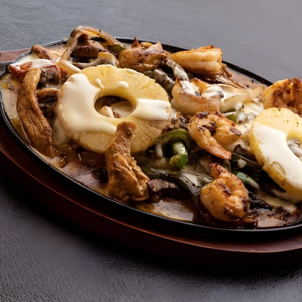 Sizzling fajitas with chicken, shrimp, pineapple, and melted cheese on a dark platter.