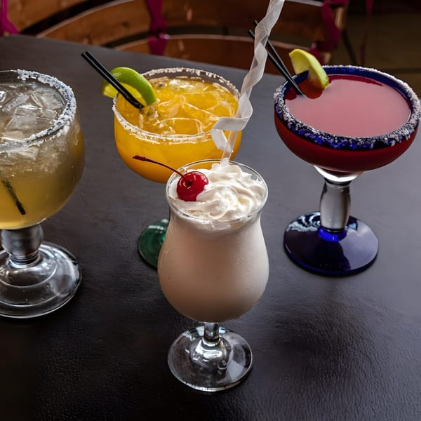 Four colorful Camila's Mexican Restaurant drinks, including margaritas and a creamy cocktail with whipped cream and a cherry.