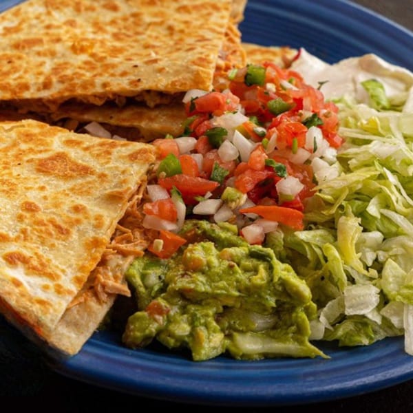 Chicken quesadillas with pico de gallo, guacamole, sour cream, and shredded lettuce on a blue plate.